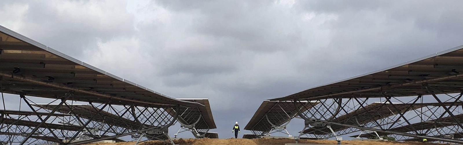 Montage de trackers photovoltaïques sur un chantier, vus de dessous, un technicien casqué au centre